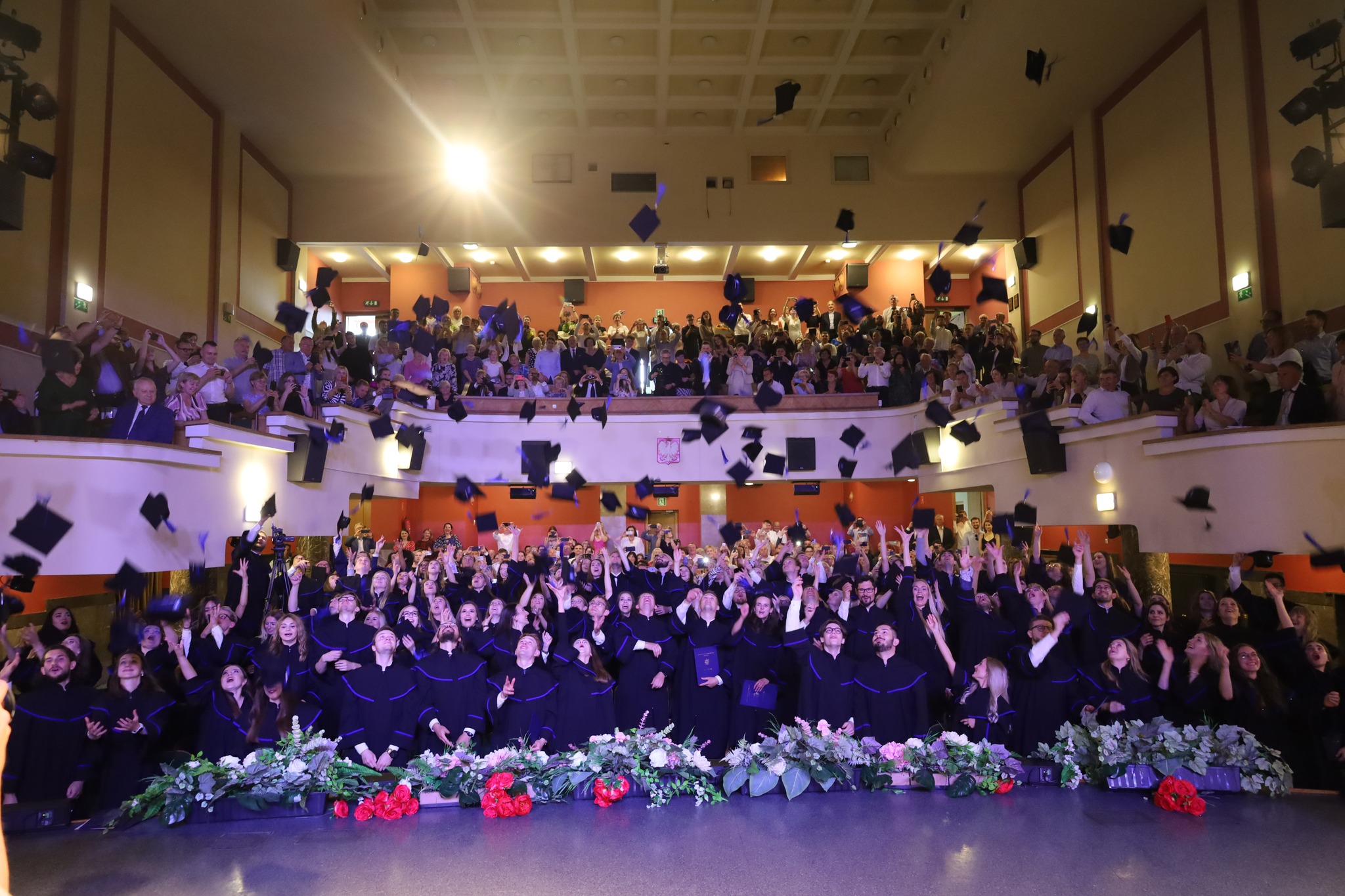 studenci podrzucają czapki do góry na sali w WDK